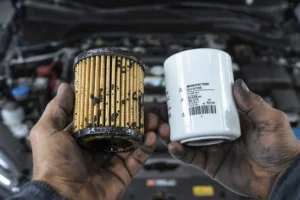 Como a Troca Correta do Filtro de Óleo Protege o Motor Mãos de um mecânico segurando um filtro de óleo sujo ao lado de um novo e limpo na frente de um motor.