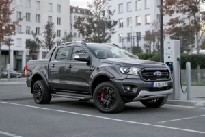 Ford Ranger MS-RT PHEV cinza escura, um veículo híbrido plug-in com suspensão rebaixada, estacionada em uma estação de recarga elétrica em Munique.